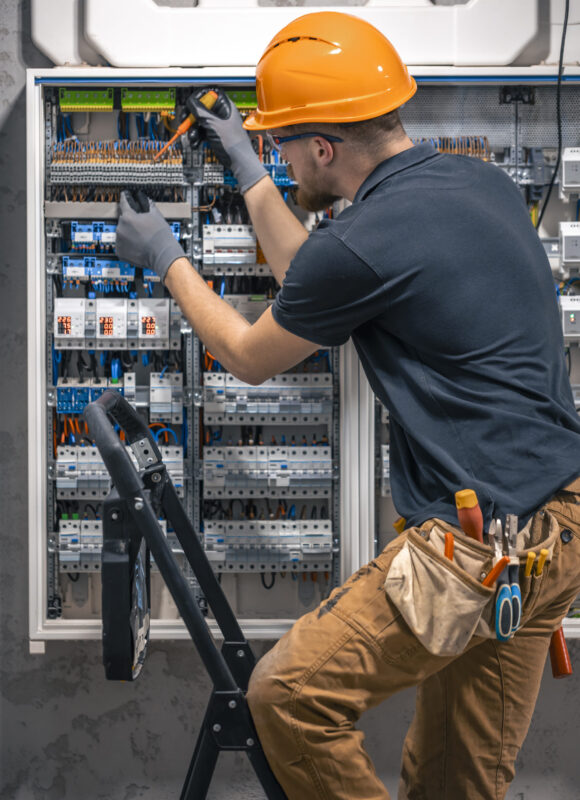 Male electrician working in a switchboard with fuses. Installation and connection of electrical equipment. Professional with tools in hand.